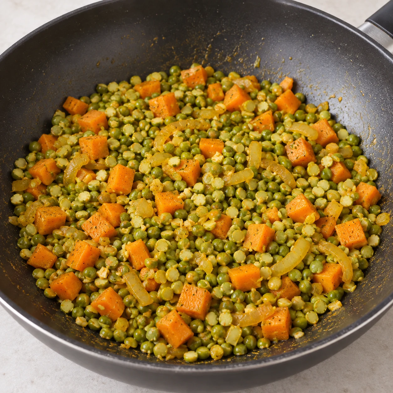 Pois cassés verts versés dans un wok de petits morceaux de carottes et oignons jaunes, aucun liquide.